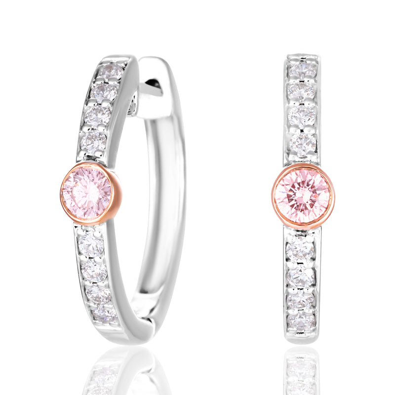 A pair of silver huggie hoop earrings with a row of clear pavé stones and a central round pink gemstone in a rose gold setting, shown on a white background with a soft reflection.