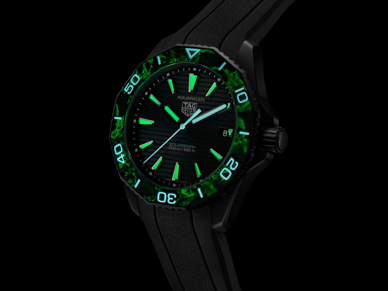 Black TAG Heuer Aquaracer Solargraph dive watch with glowing green bezel, luminous markers, blue hands, rubber strap.