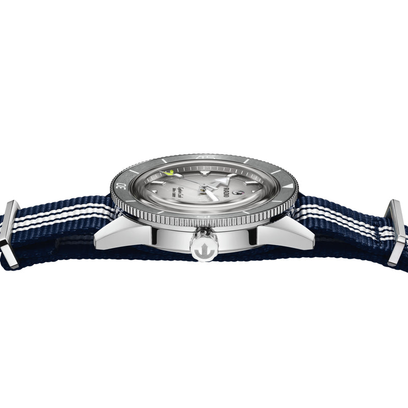 Side view of a Rado Captain Cook watch with a grey dial, polished steel case, and a navy blue NATO strap with white stripes.