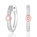 A pair of silver huggie hoop earrings with a row of clear pavé stones and a central round pink gemstone in a rose gold setting, shown on a white background with a soft reflection.