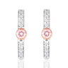 A pair of silver-toned huggie hoop earrings featuring a central round pink gemstone surrounded by a rose gold bezel, with additional clear round-cut stones set along the vertical bars, shown on a white background with a soft reflection.