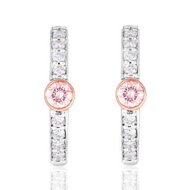 A pair of silver-toned huggie hoop earrings featuring a central round pink gemstone surrounded by a rose gold bezel, with additional clear round-cut stones set along the vertical bars, shown on a white background with a soft reflection.